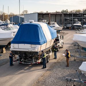 Moving Boat on a trailer at a marina yard, with crew checking height, straps, and permits before spring launch