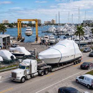 Boat Transport Fort Lauderdale truck hauling a yacht near marina lifts with busy port access in the background